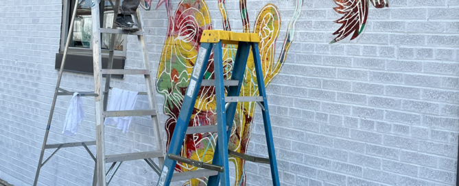 Richie Morales on a ladder next to a mural in progress