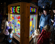 Children and adults look at a glowing lite brite structure with pegs spelling out science