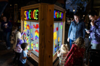 Children and adults look at a glowing lite brite structure with pegs spelling out science