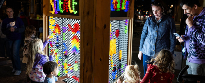 Children and adults look at a glowing lite brite structure with pegs spelling out science